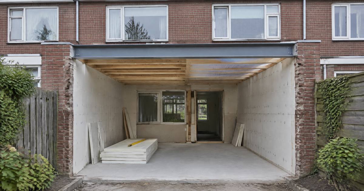Een uitbouw in aanbouw achter een rijtjeshuis: een stalen balk boven de brede opening, isolatieplaten tegen de muren en open dakbalken. Illustratie.